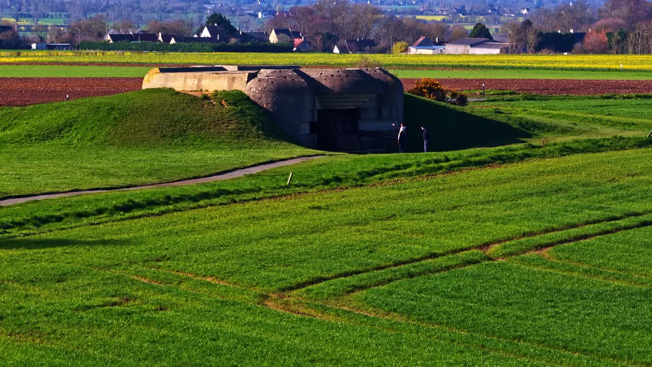 En historisk bunker fra Anden Verdenskrig ligger midt i frodige grønne marker i Longues-sur-Mer. Perfekt til historiedokumentarer eller undervisningsmateriale.