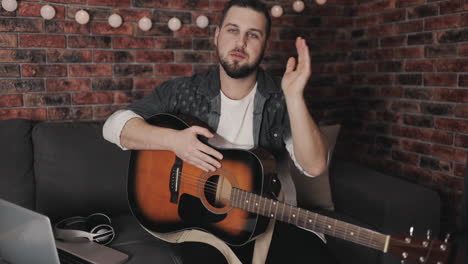 joven músico masculino grabando y transmitiendo un video tutorial, tocando la guitarra en casa