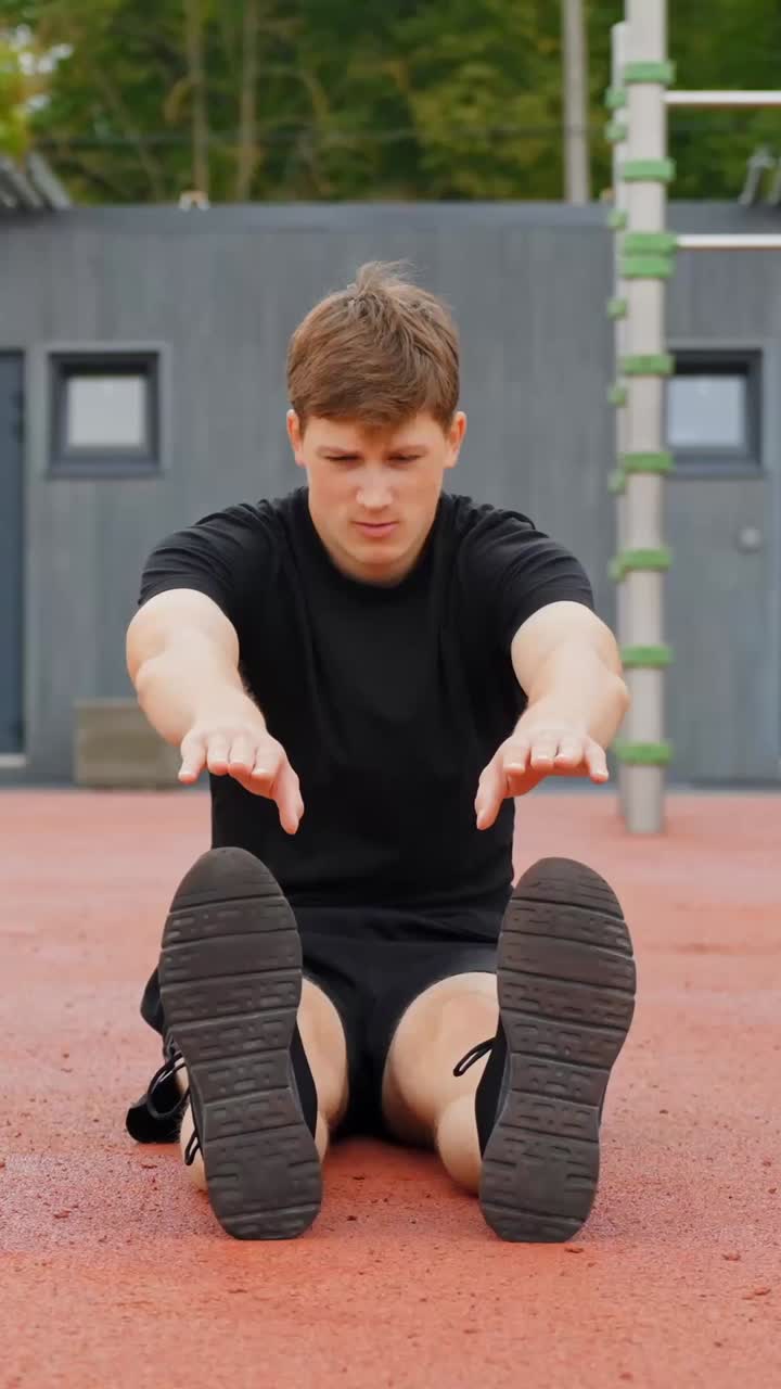 Man Doing Seated Forward Fold - Stretching, Sitting On The Ground With His Legs Straight And Reaching For His Toes. - vertical shot