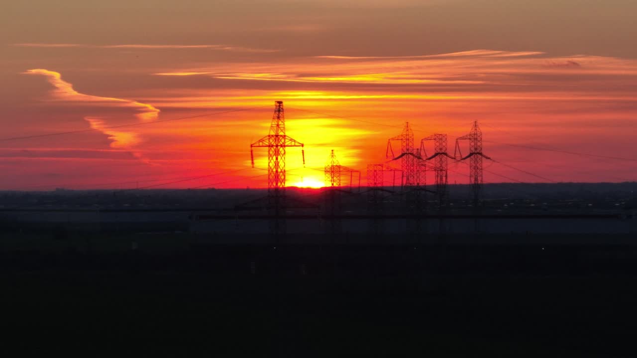 황금빛 일몰 앞 전기 철탑의 실루엣을 보여주는 공중 와이드 샷