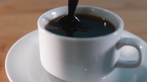 close interior shot of stirring black coffee with metal spoon at night