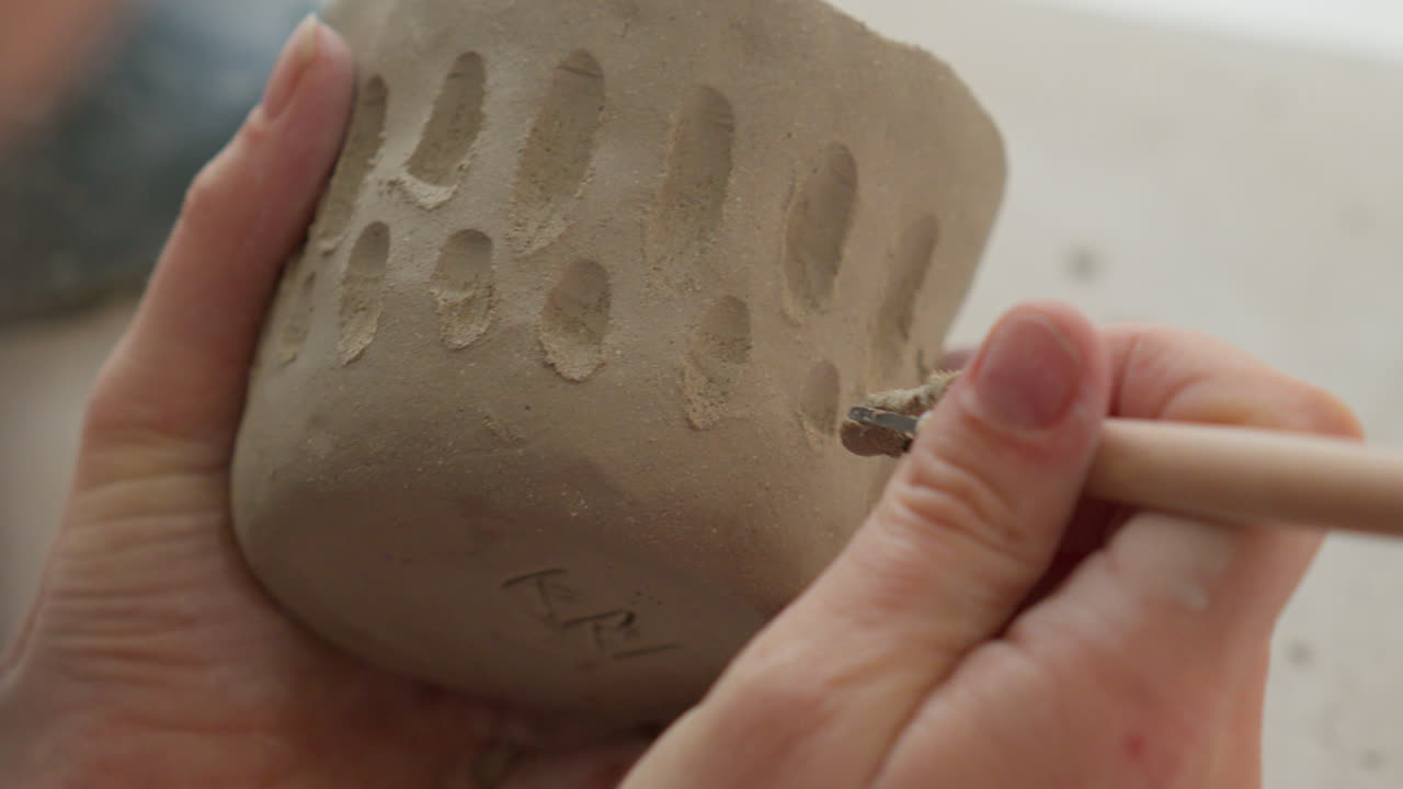 Etching intricate designs into soft clay with a specialized tool, showcasing artisan's delicate touch