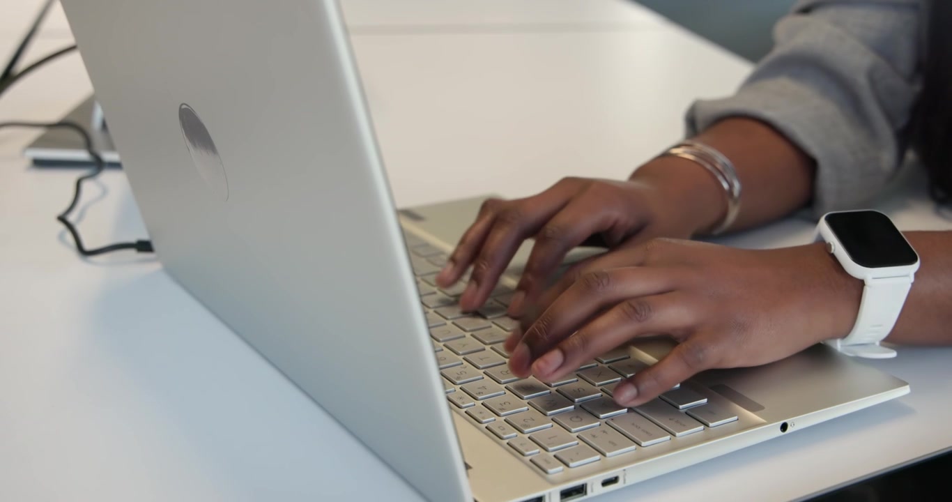 Les mains d'une femme planent puis tapent sur un ordinateur portable argenté à un bureau, terminant un document de travail.