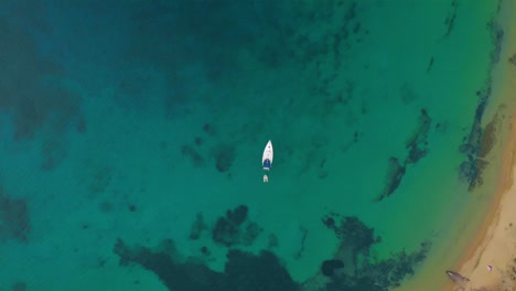 Drone-shot-above-a-sail-boat-on-the-blue,-Mediterranean-sea,-on-the-coast-of-Mykonos,-in-Greece---top-down,-aerial-view