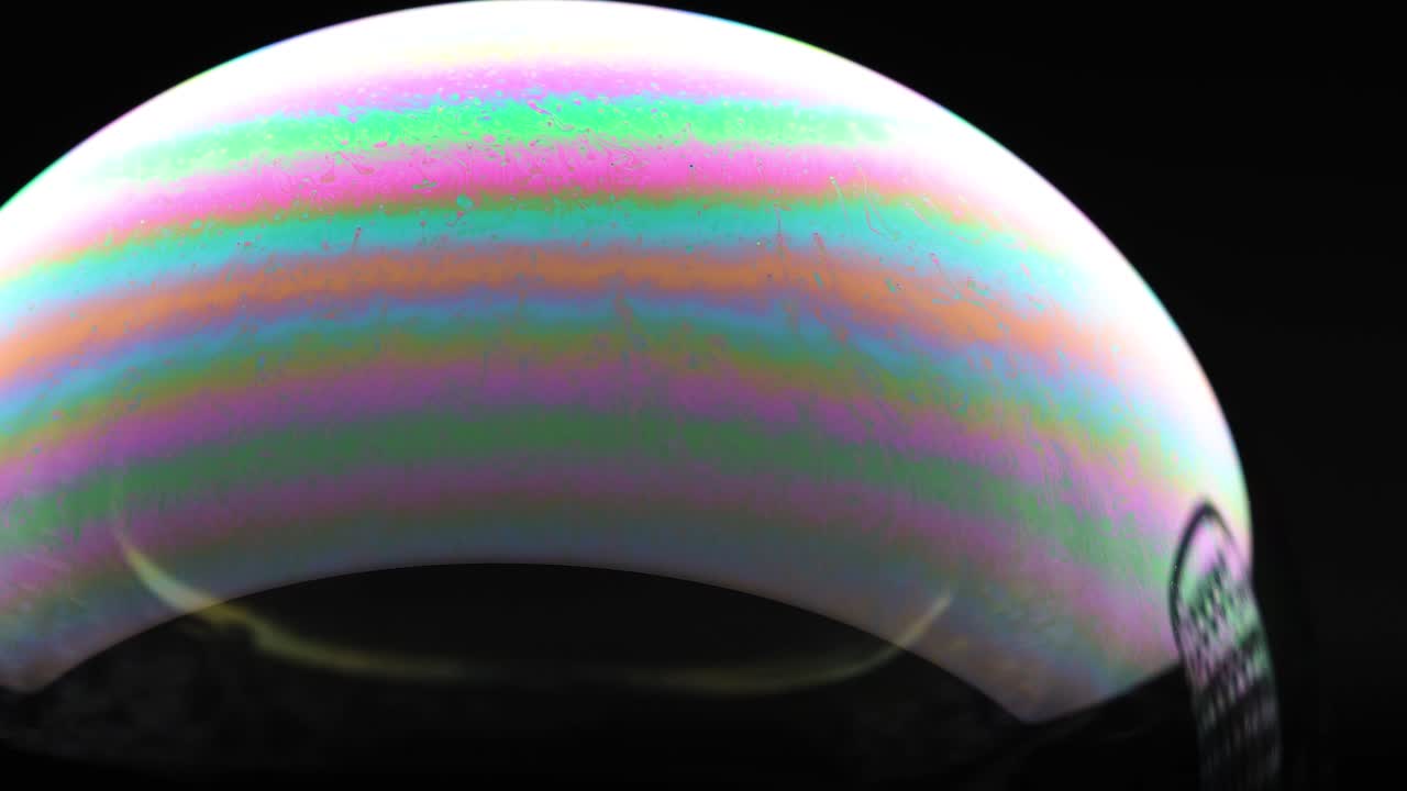 Close-up of a soap bubble with vibrant color reflections under dark lighting, showcasing dynamic surface patterns