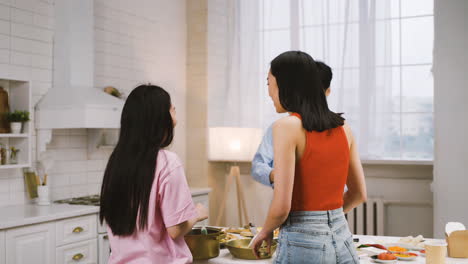 부엌에서 요리하는 동안 세 명의 일본 친구가 팬에 재료를 붓는다