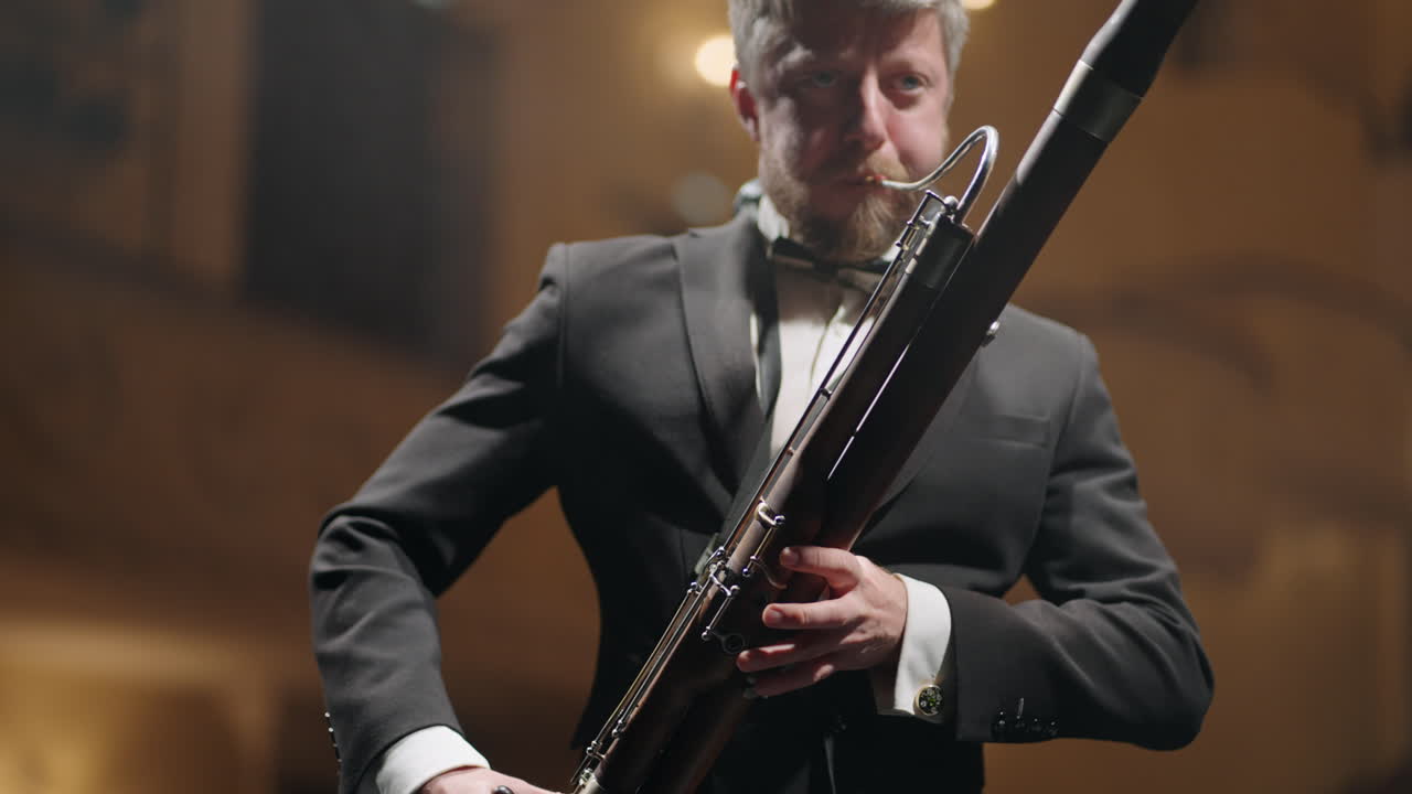 파소니를 들고 있는 남자가 클래식 음악 홀의 장면에서 음악을 연주하고 있습니다. 검은 옷을 입은 음악가입니다.