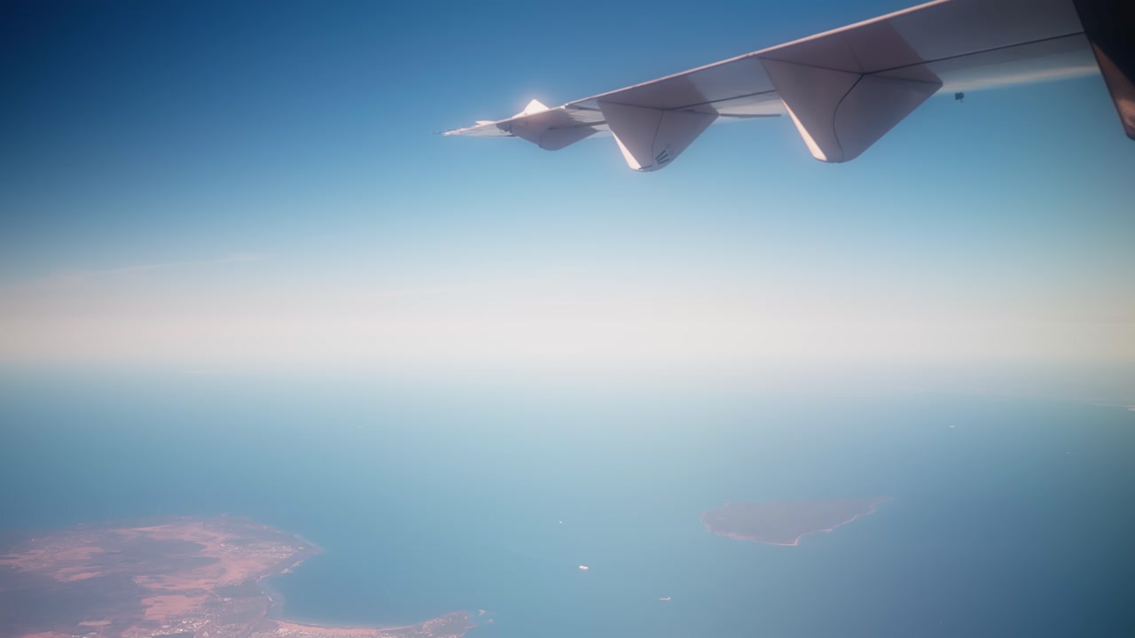 Airplane wing above open sea and distant islands, capturing high-altitude coastal travel, clear blue airspace, and a wide passenger view from the sky.