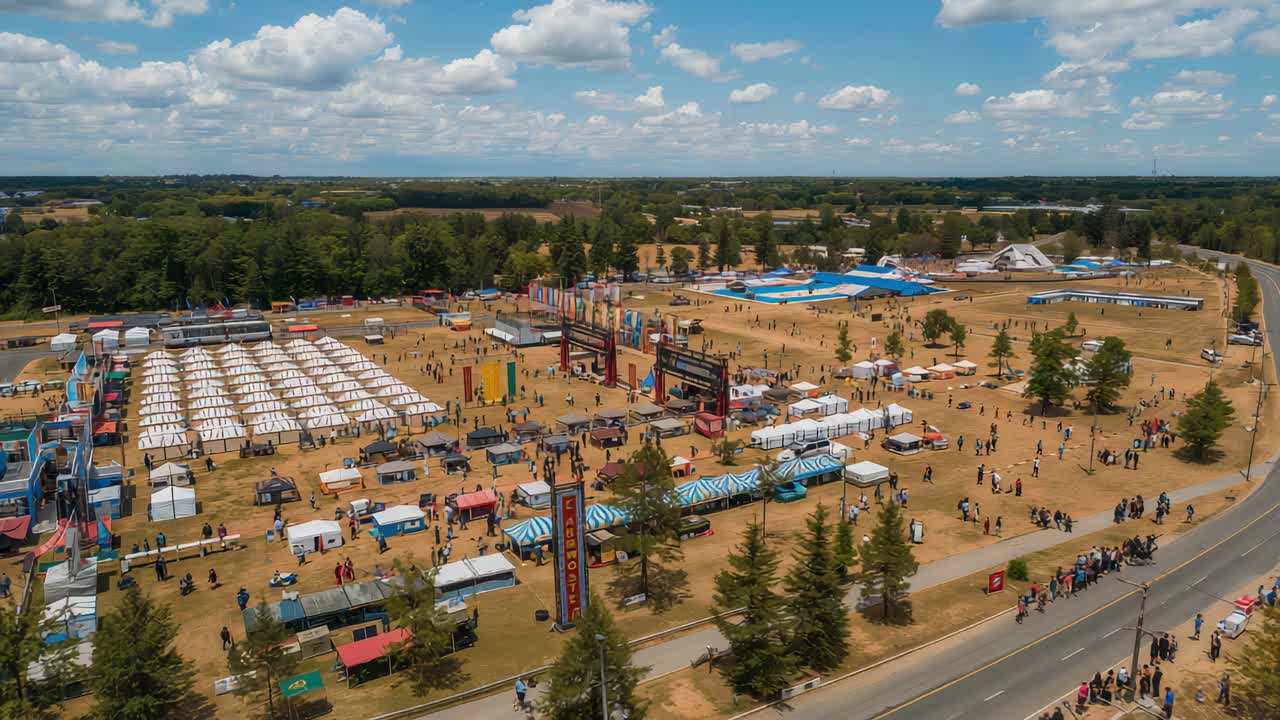 Schwenkdrohne, die das Festivalgelände für eine Luftaufnahme erfasst und weiße Zelte, eine Bühne und Mitarbeiterwesten zeigt