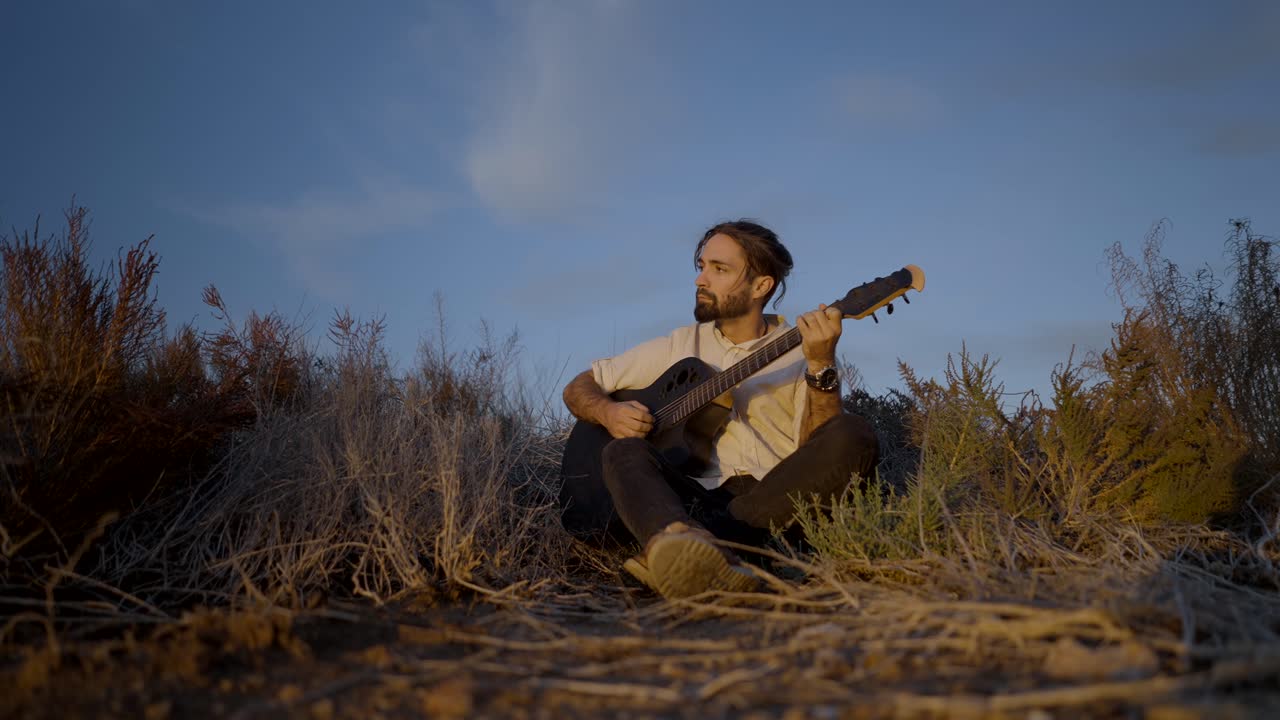 Mand spiller guitar på en mark ved solnedgang