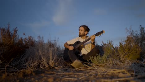 man playing guitar in a field at sunset