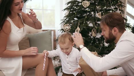 Blonde-cute-toddler-receiving-christmas-present-from-his-father.-Beautiful-christmas-tree-on-the-background.-Family-christmas