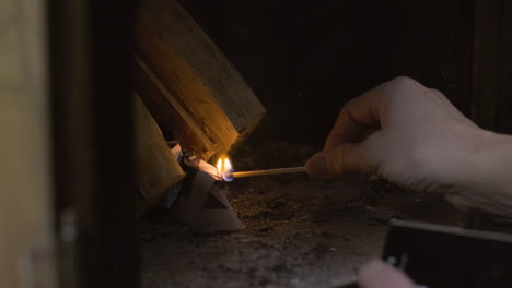 close up of old elderly caucasian woman lady grandma hands lighting a wooden match to light a cozy warm fire in a fireplace oven stove in a cabin during snowy cold christmas xmas celebration warmth