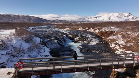 snowy aerial - brúarfoss waterfall bridge with woman standing laugarvatn iceland
