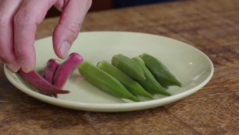 Green-and-red-okra-being-placed-on-a-white-plate,-close-up-shot