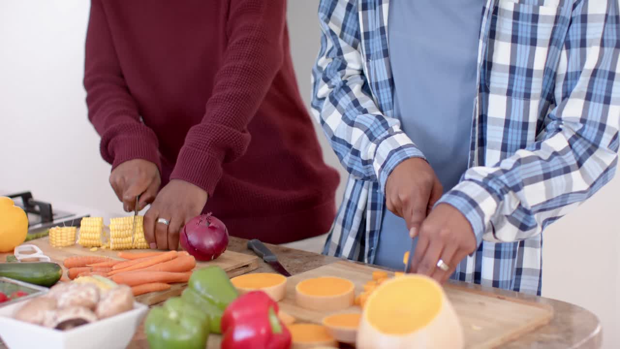 Happy african american gay male couple preparing dinner, chopping vegetables in kitchen, slow motion