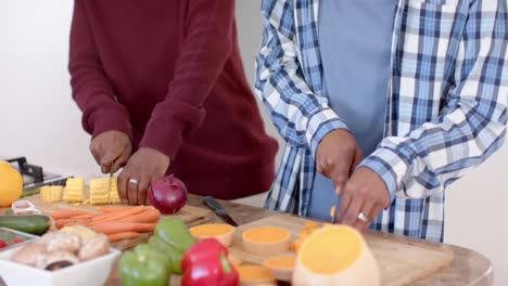 Happy-african-american-gay-male-couple-preparing-dinner,-chopping-vegetables-in-kitchen,-slow-motion