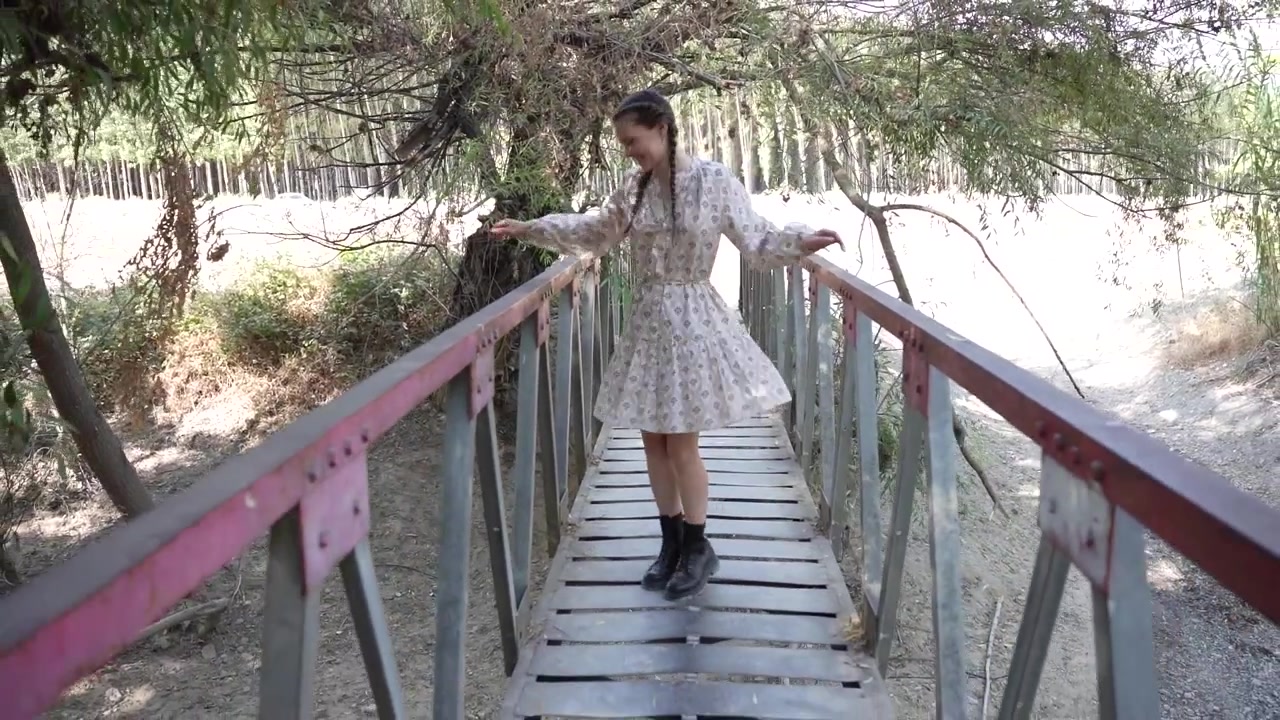 Una giovane donna gioiosa che danza con gioia su un affascinante ponte rustico circondata dalla natura.