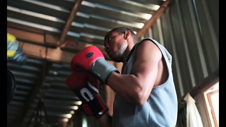 Pugile uomo afroamericano che pratica boxe con l'allenatore in palestra 4K