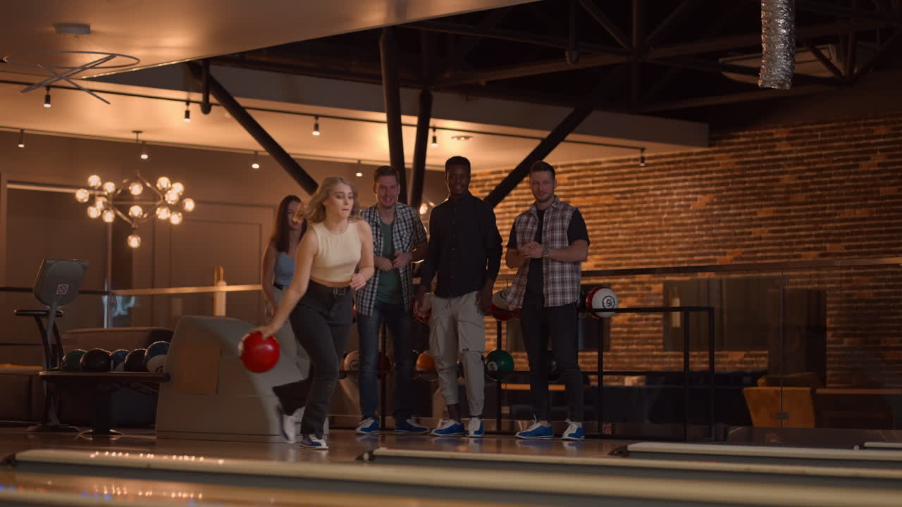 plano geral um jovem em uma camisa jogador de boliche lança uma bola com o apoio de amigos e se alegra por nocautear uma tira
