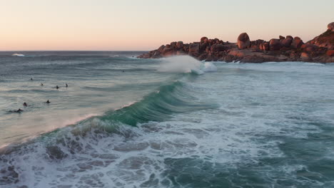 Leute,-Die-Surfen-Und-Wellen,-Die-An-Die-Küste-Krachen,-Erzeugen-Meeresschaum-Bei-Sonnenuntergang-In-Llandudno-Beach,-Kapstadt,-Südafrika---Kamerafahrt