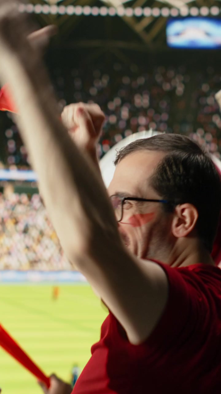 Video vertical: Vista trasera de diversos aficionados al fútbol celebrando en las gradas del estadio