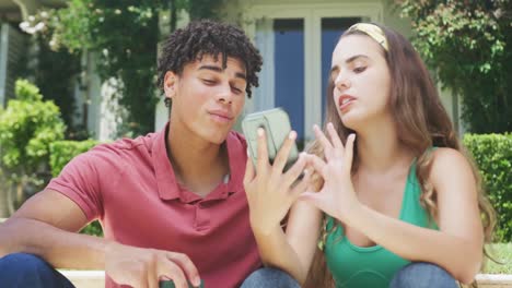 feliz pareja biracial pasando el tiempo en el jardín hablando con el teléfono inteligente