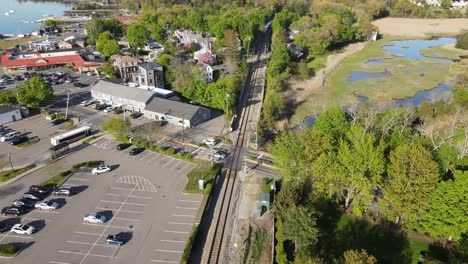 Drone-rising-to-reveal-Amtrak-train-chugging-into-the-woods-in-Hingham,-a-coastal-village-in-MA,-USA