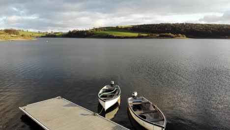 aerial low flying over wimbleball lake on exmoor in somerset with empty boats beside pier