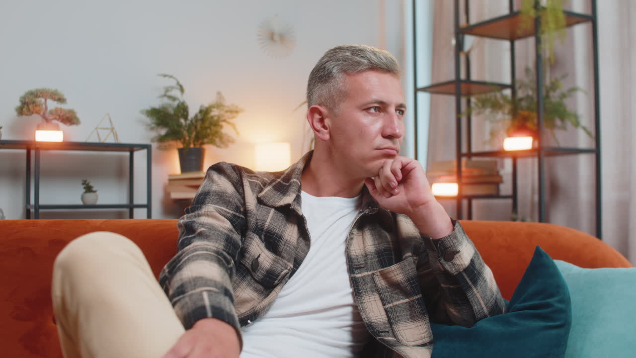 Thoughtful man rubbing chin looking aside with pensive expression pondering a solution at home room