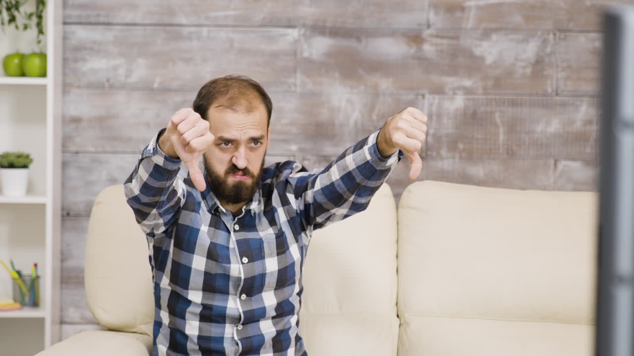 Worried man watching TV showing thumbs down