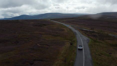Aerial-panoramic-footage-of-large-moorlands.-Tracking-of-car-driving-on-road.-Cloudy-sky-over-highlands.-Ireland