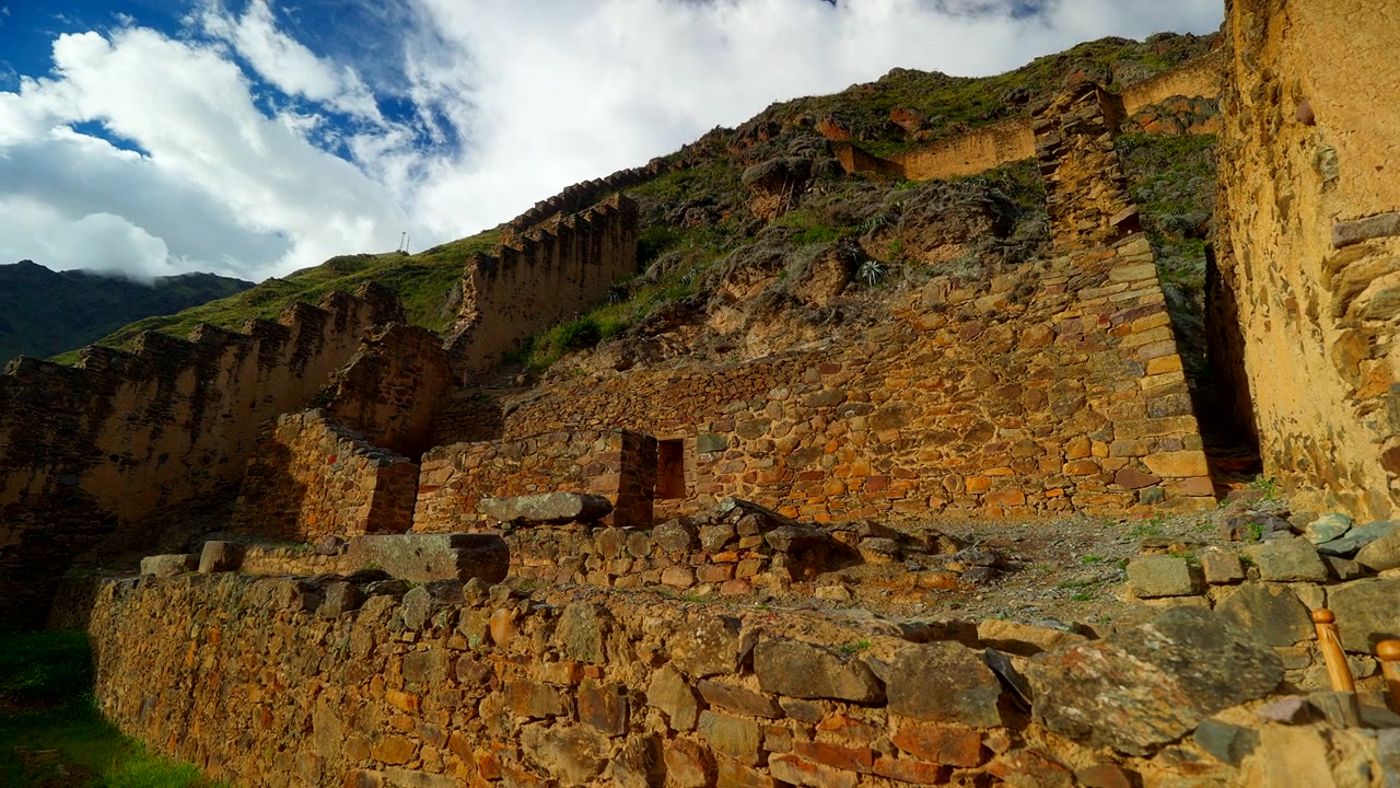 Antiche rovine in pietra e adobe si ergono su un ripido pendio a Ollantaytambo, Valle Sacra, Perù, panoramica media a sinistra di presentazione alla luce dorata del tramonto.