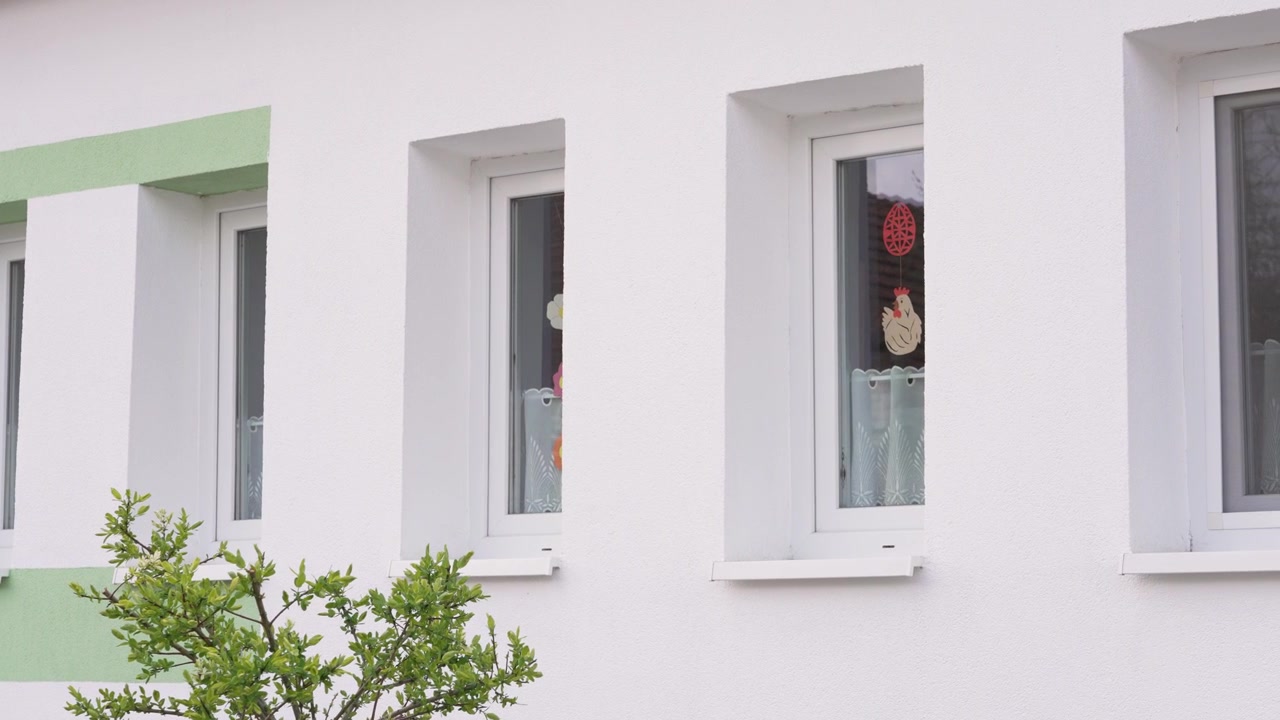 Children's Easter decorations hanging inside a kindergarten window on a white building facade