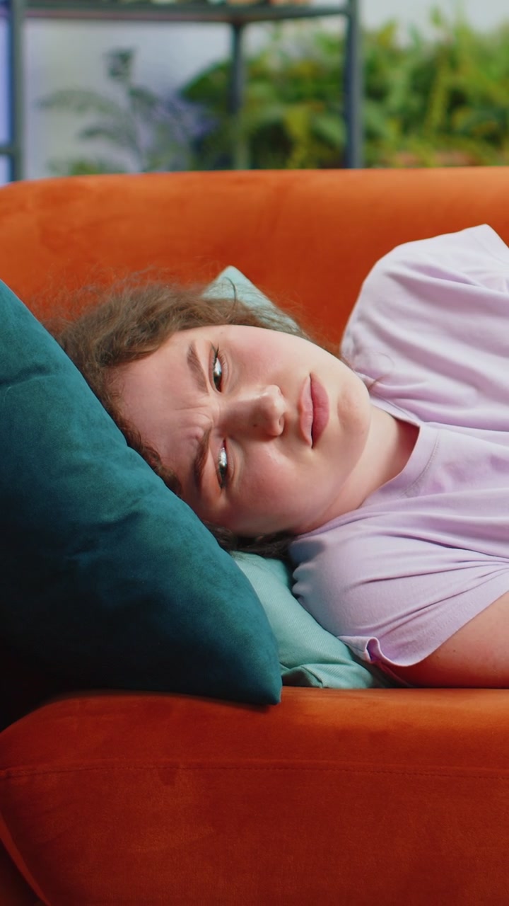 Sick ill woman suffering from period cramps stomach ache menstrual pain lying on sofa at home room