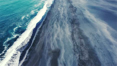 drone flying over a large black beach with the camera tilting down slowly over shore in iceland 4k