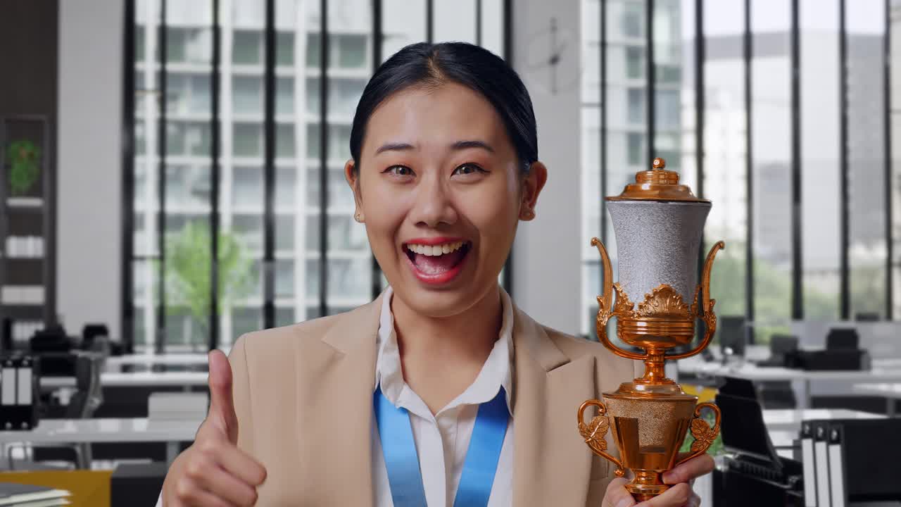Close Up Of Asian Business Woman In A Suit With A Gold Medal And Trophy Showing Thumbs Up Gesture And Smiling To Camera As The First Winner In The Office