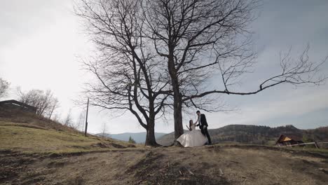 Newlyweds.-Caucasian-groom-with-bride-ride-a-rope-swing-on-a-mountain-slope