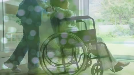 Animation-of-spots-over-asian-nurse-with-woman-in-wheelchair