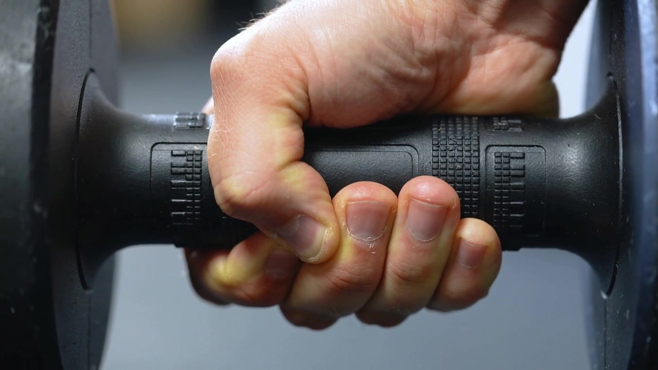 Gripping adult hand maintaining hold while preparing to lift at gym, with textured dumbbell handle