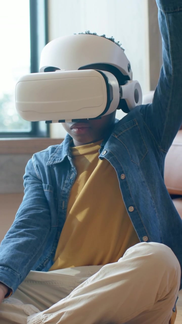 Video verticale: Bambino in jeans che reagisce all'attivazione di un visore VR bianco, giocando a un gioco virtuale in soggiorno.