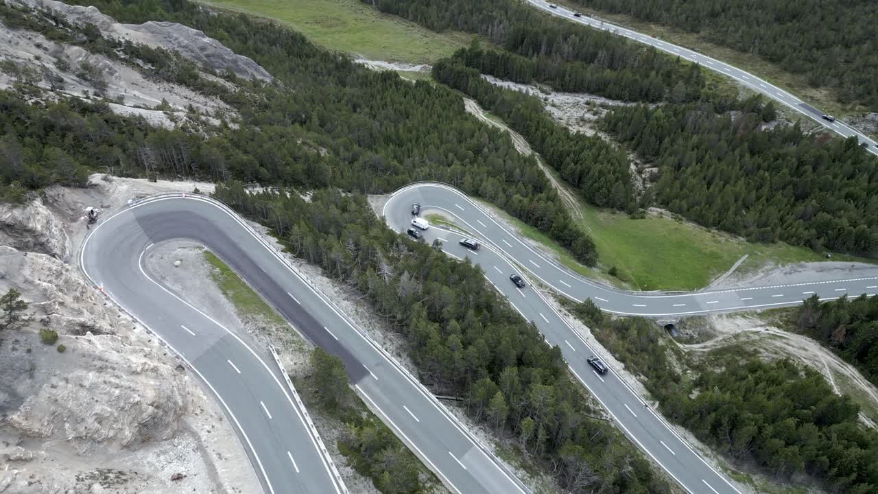 Fly-up tilt-down drone view of cars driving tight curves on alpine forest road