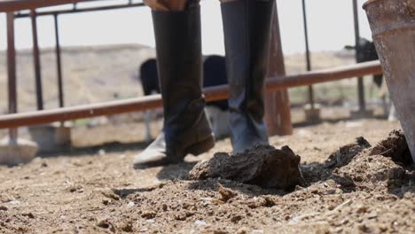 primer plano de las botas de los agricultores mientras se echa tierra y estiércol en un cubo de metal