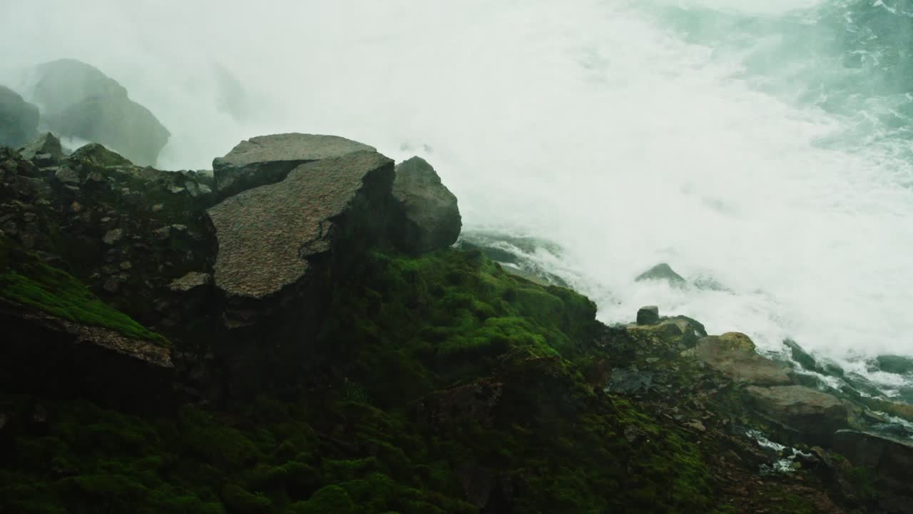 Cracked slabs and mossy rocks sit at the base of Niagara Falls, surrounded by mist and cascading water, capturing raw beauty and erosion