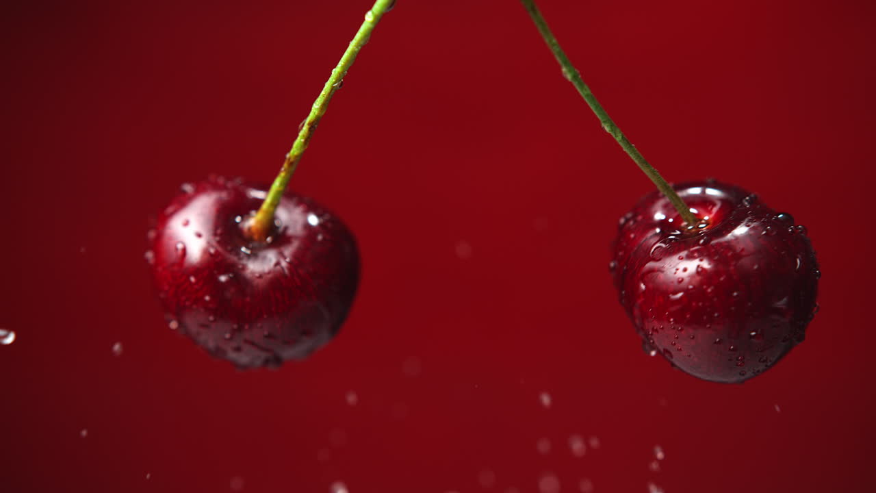 Ciliegie dolci con gambo che si scontrano e schizzano goccioline d'acqua sullo sfondo rosso, macro e al rallentatore