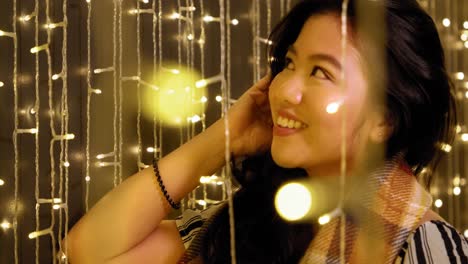 beautiful young asian filipina woman smiling and adjusting hair in warm yellow fairy lights in 4k slow motion