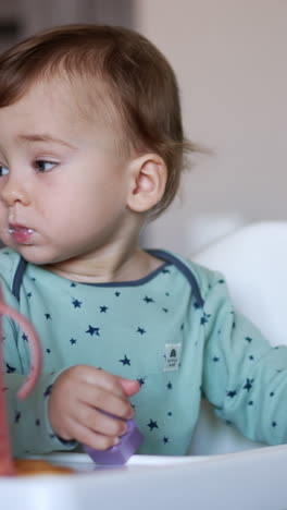 cute adorable baby boy sitting in the feeding chair. caucasian child with smeared face playing with a toy. blurred backdrop. vertical video