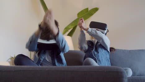 Happy-boy-and-girl-sitting-on-sofa-and-playing-videogame-with-VR-glasses