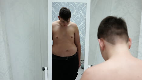 young fat man looking at his mirror reflection and shaking his belly