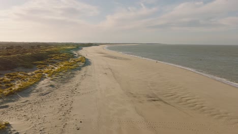 Toma-Aérea-De-Una-Playa-Vacía-Y-Dunas-Verdes-En-Una-Reserva-Natural-Al-Atardecer